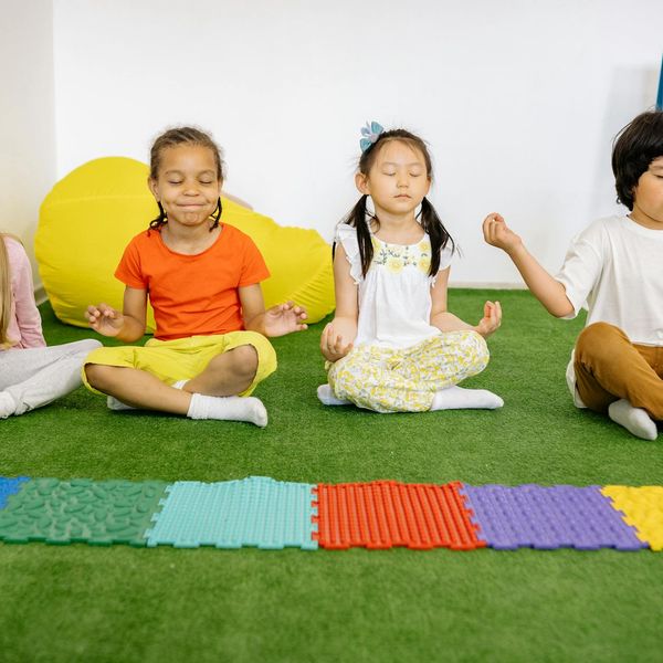 A diverse group of kids laughing while trying a partner yoga pose.